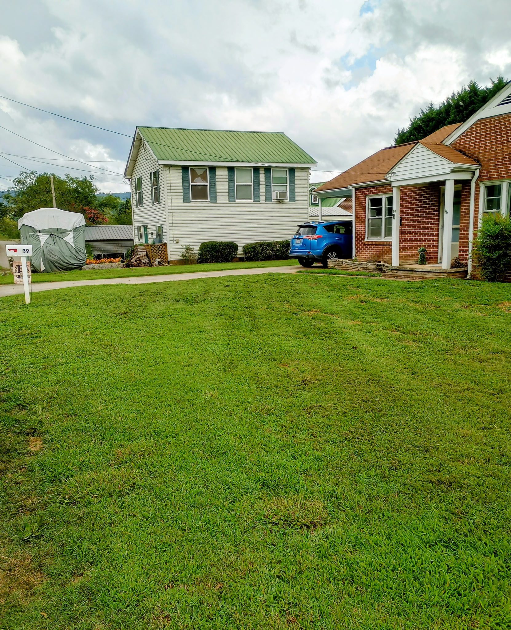 A green lawn between two houses with a blue car parked on the right.