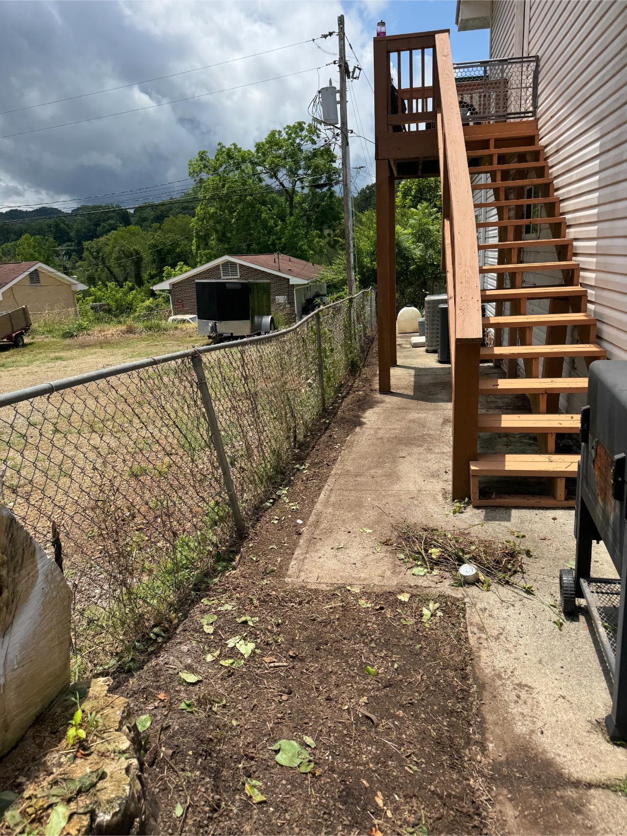 A backyard with a dirt path alongside a wooden staircase and chain-link fence.