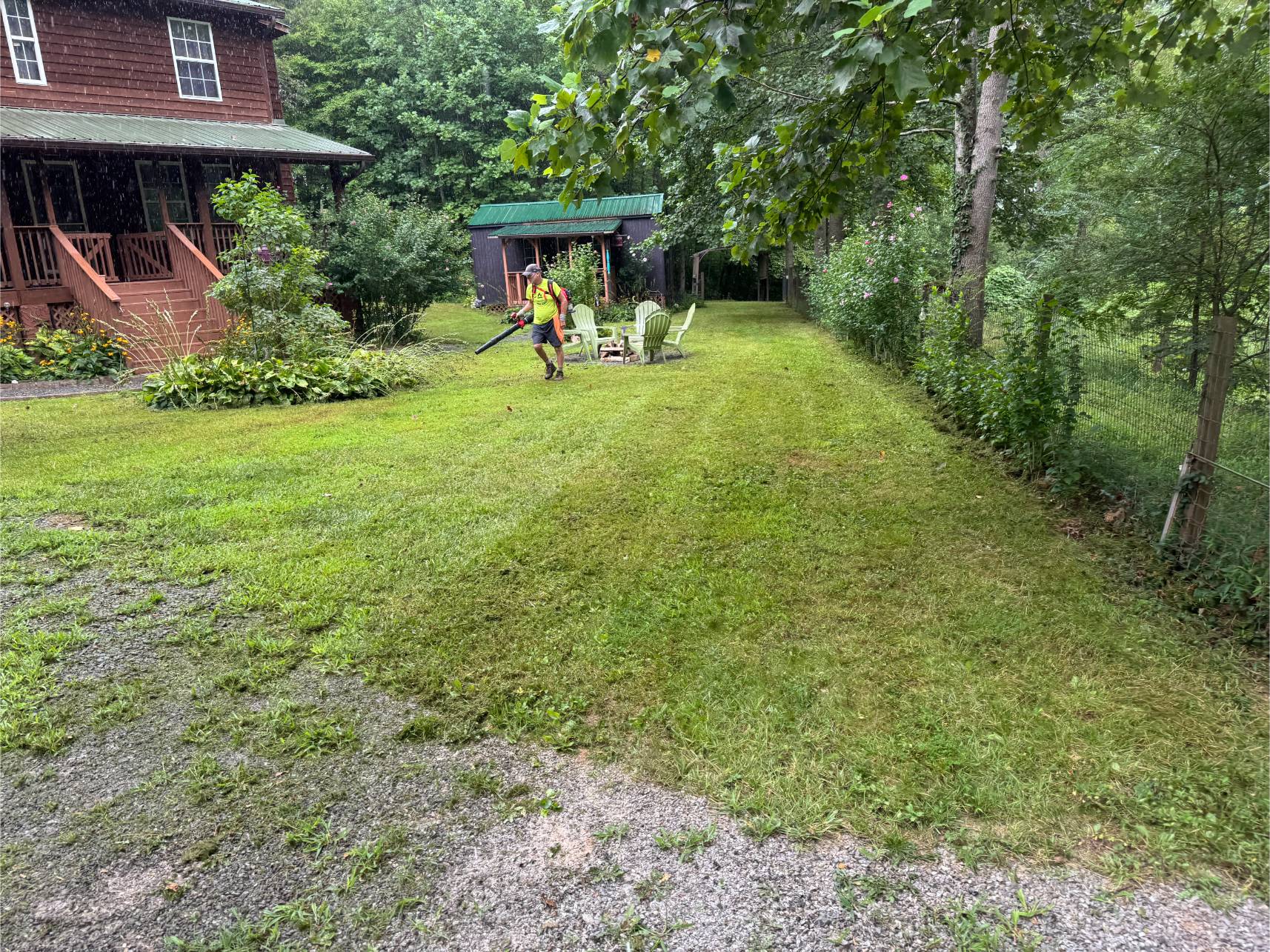 A green lawn with chairs and a gazebo in a backyard surrounded by trees.