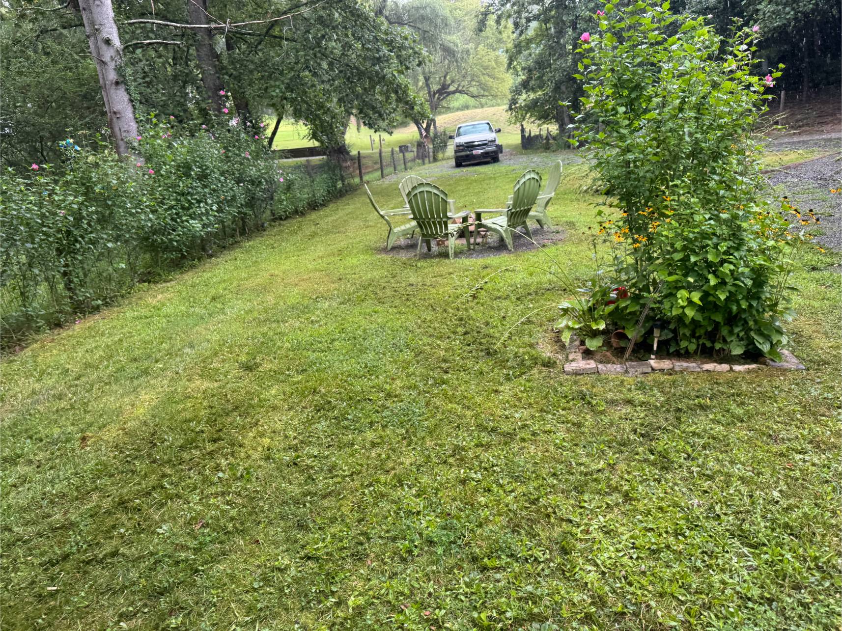 A neatly mowed backyard with two chairs and a table near a small tree.